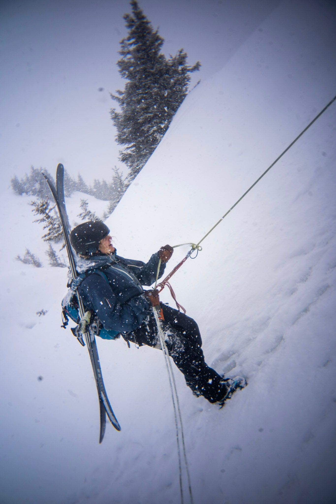 Freerider seilt sich mit Ski am Rucksack im Schneefall ab