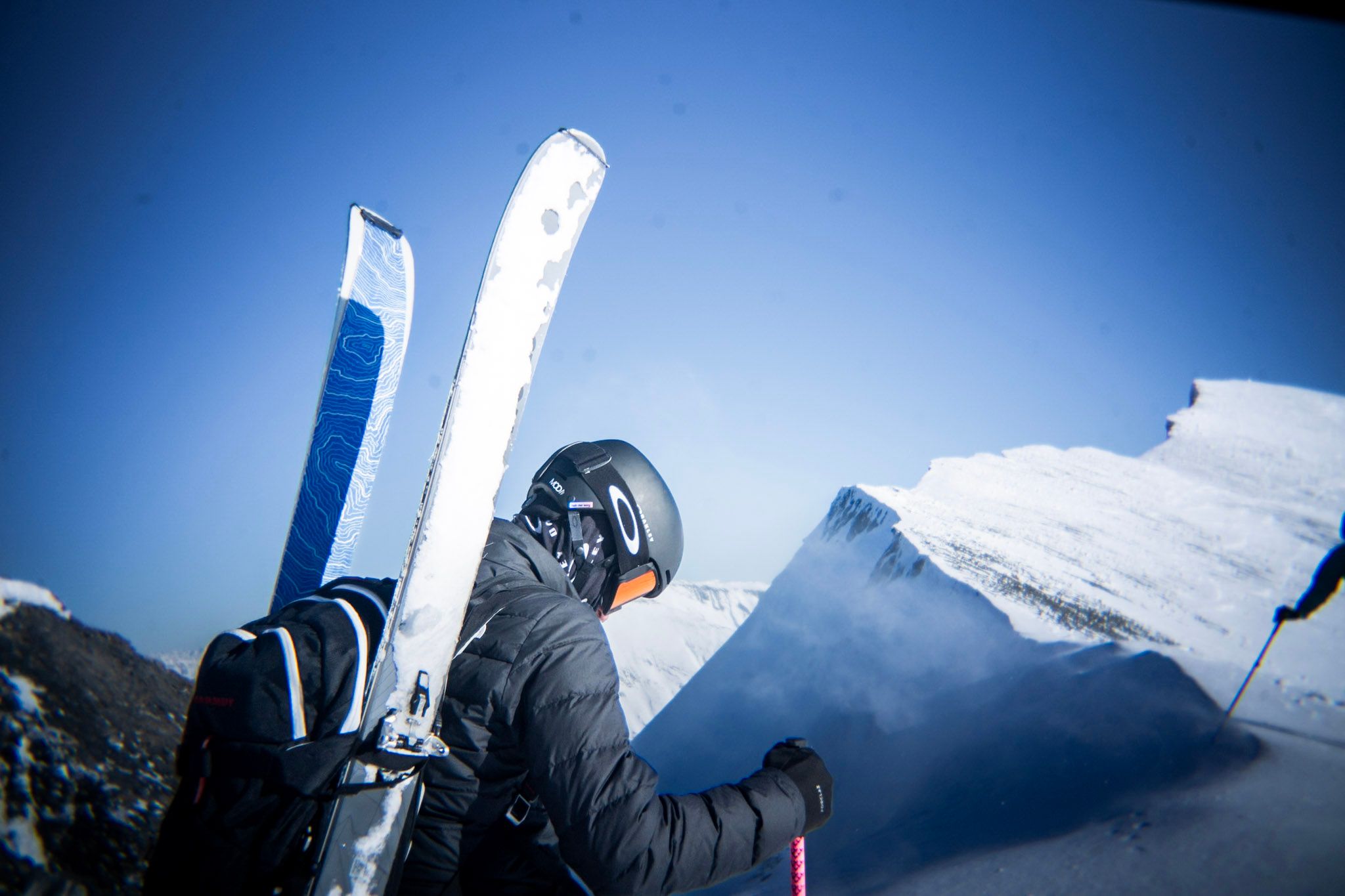 Freerider steht auf einem Grat, die Ski am Rucksack befestigt