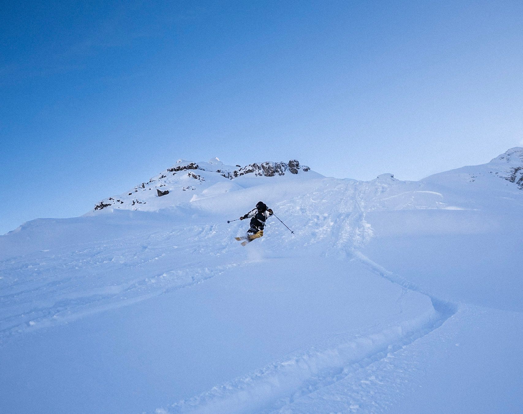 Skifahrer zieht Schwünge durch eine offene Pulverschneemulde unter Felsgipfeln