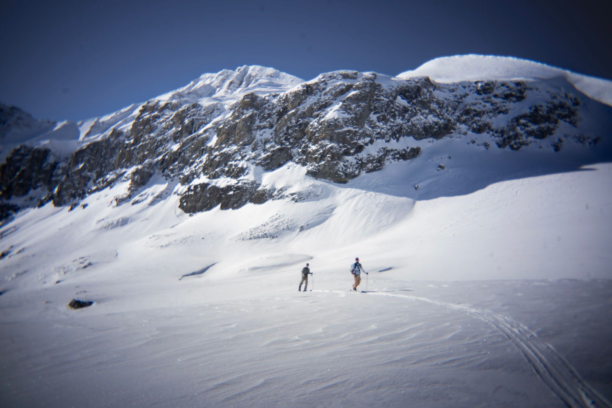 Zwei Skifahrer steigen mit Fellen unterhalb einer grossen Felswand auf